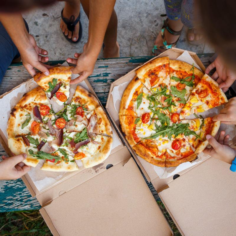Hands reaching for slices from two pizzas on a table